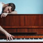 Melancholic pianist playing piano near blue wall